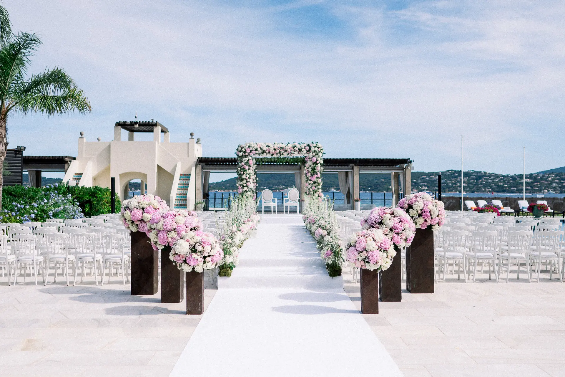 Cérémonie de mariage au bord de l'eau, chaises blanches et arche fleurie