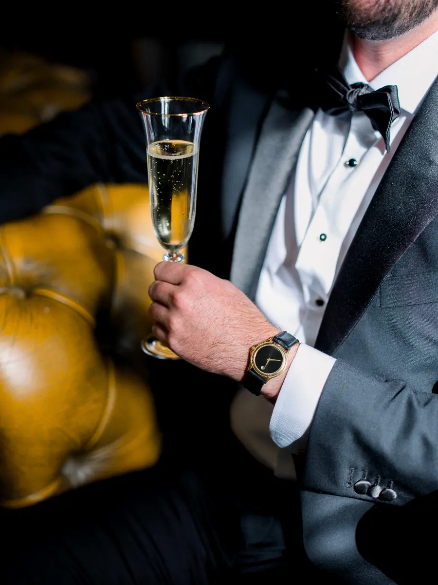 Détail mariage éditorial – marié en smoking tenant une coupe de champagne