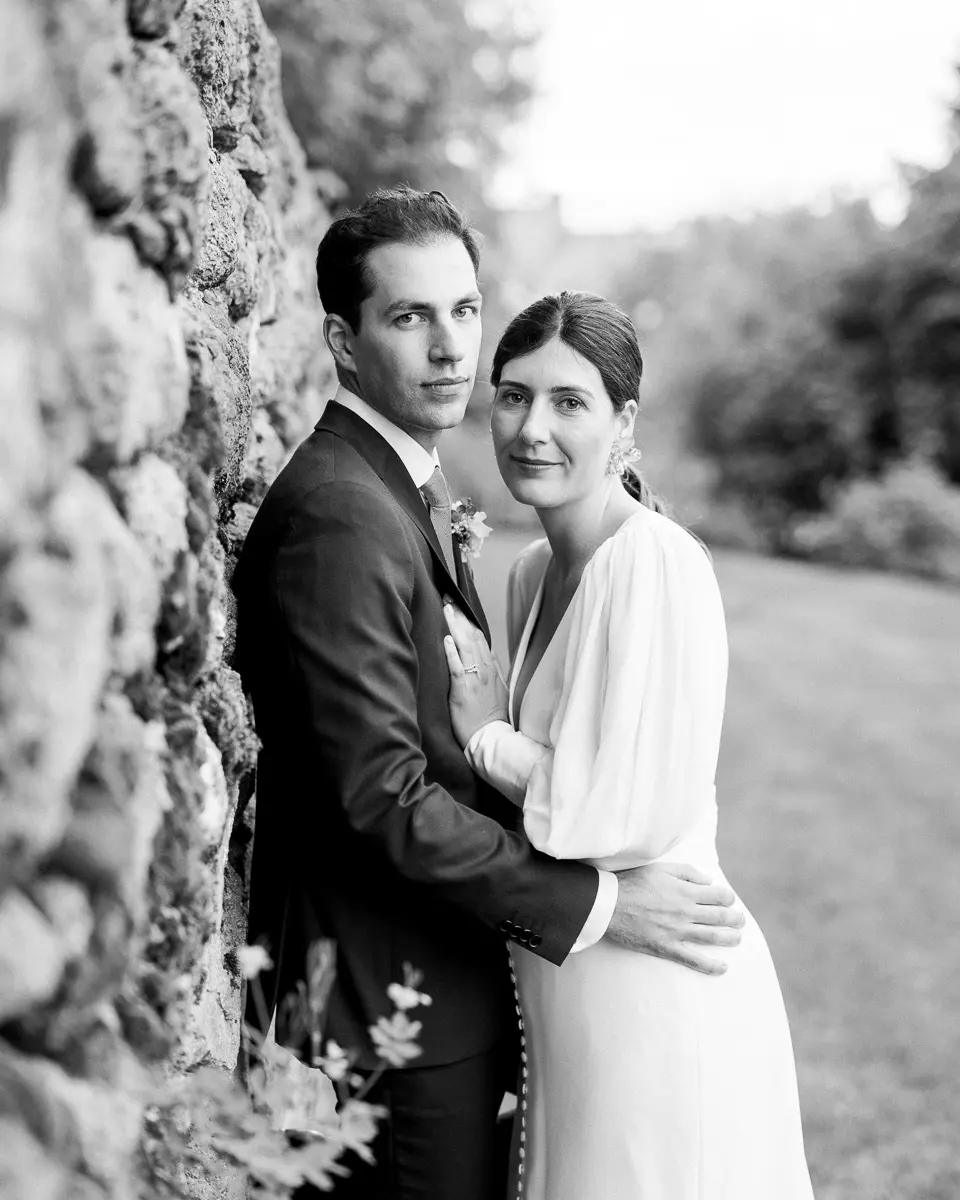 couple de mariés posant près d’un mur en pierre photographie de mariage élégante par Tristan Perrier