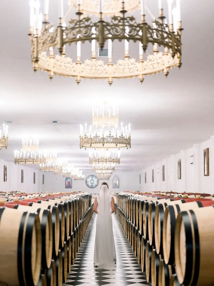 mariée marchant entre les barriques d’un chai viticole en Gironde – photographie de mariage