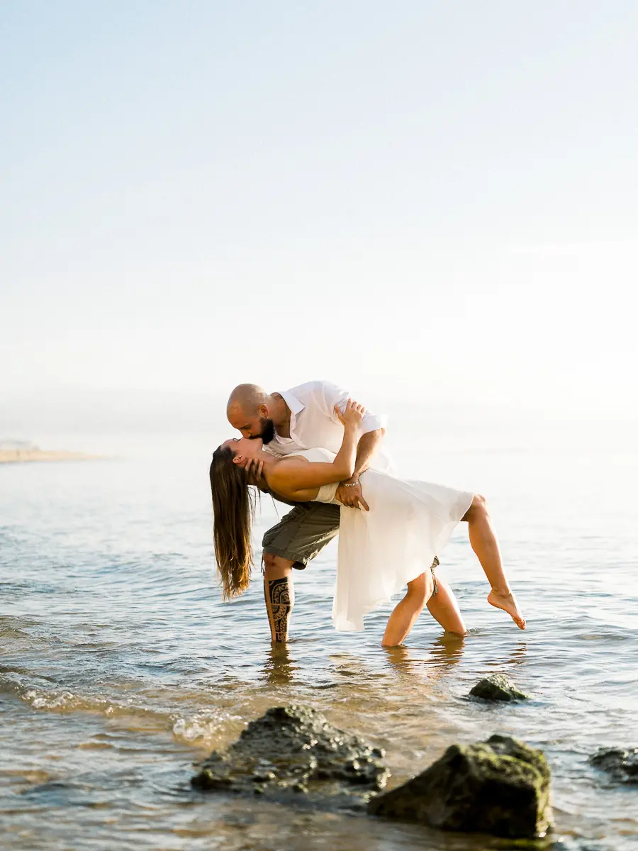 Couple enlacé dans l’eau lors d’une séance engagement sur la plage au coucher du soleil